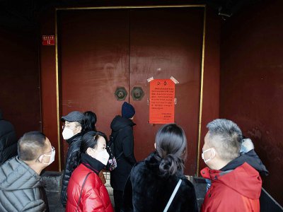 Des Chinois, un masque de protection sur le visage, devant la porte du Temple des Lamas fermé pour éviter la propagation du nouveau coronavirus, le 25 janvier 2020 à Pékin - NOEL CELIS [AFP]