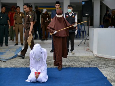 Une éxécutrice sur le point de flageller en public une femme agenouillée, le 10 décembre 2019 à Aceh, en Indonésie - CHAIDEER MAHYUDDIN [AFP]