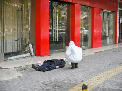 Un membre des services de secours examine le corps d'un homme mort dans la rue à Wuhan, le 30 janvier 2020 en Chine - Hector RETAMAL [AFP]
