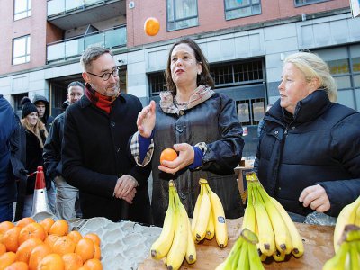 Mary Lou McDonald (c), la cheffe du Sin Fein, jongle avec des oranges en parlant avec une vendeuse de fruits (d), le 10 février 2020 à Dublin - PAUL FAITH [AFP]