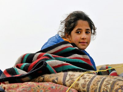 Une fillette syrienne assise sur les affaires transportées par sa famille qui fuit les combats, dans la région d'Alep (Syrie), le 14 février 2020 - Rami al SAYED [AFP]