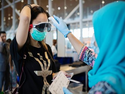 Une hôtesse de l'air de Malaysia Airlines prend la température d'une passagère chinoise à l'embarquement d'un vol pour Pékin, le 14 février 2020 à l'aéroport de Kuala Lumpur - NICOLAS ASFOURI [AFP]