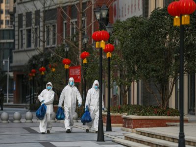 Des employés en combinaison de protection livrent des sacs de nourriture aux habitants d'un quartier de Wuhan, le 20 février 2020 en Chine - STR [AFP]