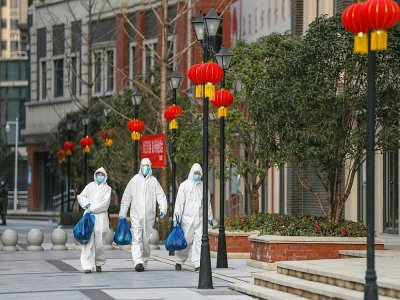 Des employés en combinaison de protection livrent des sacs de nourriture aux habitants d'un quartier de Wuhan, le 20 février 2020 en Chine - STR [AFP]