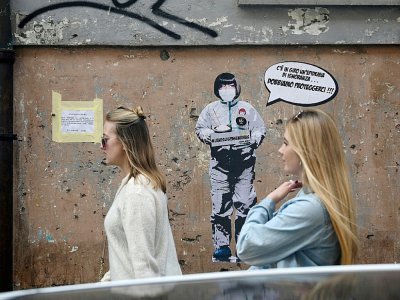 Deux femmes passent devant un message mural où il est écrit: "Il y a une épidémie d'ignorance dans l'air, nous devons nous protéger", par l'artiste Laika, près du quartier chinois de Rome, le 4 février 2020 - Filippo MONTEFORTE [AFP/Archives]