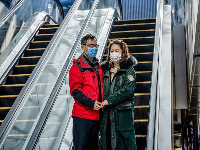 Un couple portant des masques de protection, devant un centre commercial désert, à Pékin le 22 février 2020 - NICOLAS ASFOURI [AFP]