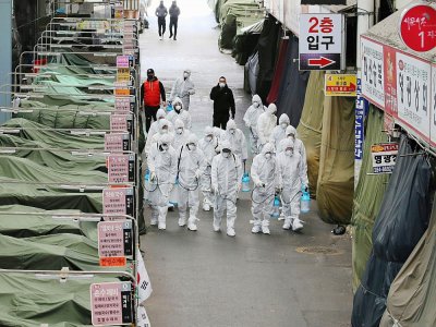 Des employés en combinaison de protection pulvérisent du désinfectant dans les allées d'un marché de la ville de Daegu, le 23 février 2020 en Corée du Sud - - [YONHAP/AFP]