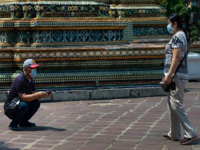 Des touristes portent des masques de protection, le 23 février 2020, devant un temple de Bangkok - Alex OGLE [AFP]