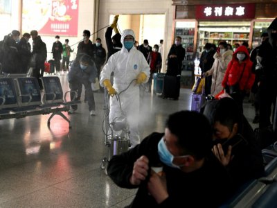 Des passagers se protègent alors qu'un homme désinfecte le hall de la gare de la ville de Hefei (province de l'Anhui), le 4 mars 2020 - Noel Celis [AFP]