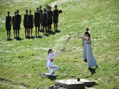 La Grecque Anna Korakaki (à genou), reçoit la torche de la flamme olympique, lors d'une cérémonie officielle devant une poignée de spectateurs à Olympie, le 12 mars 2020 - ARIS MESSINIS [AFP]