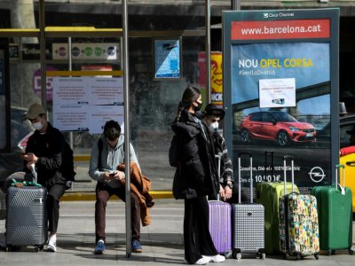 Des touristes portant des masques attendent le bus pour l'aéroport, à Barcelone (Espagne) le 15 mars 2020 - Josep LAGO [AFP]