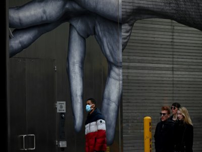 Un homme marche devant une fresque murale à New York, le 14 mars 2020 - Johannes EISELE [AFP]