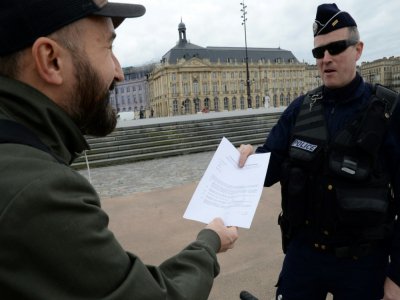 Un policier contrôle le laisser-passer d'un habitant à Bordeaux, le 17 mars 2020. Le confinement de la population est un moyen important de lutte contre la propagation de l'épidémie de coronavius - MEHDI FEDOUACH [AFP]