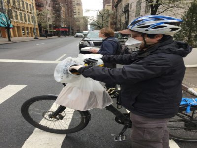 Un livreur porte masque, gants et sacs en plastique pour se protéger les mains sur son vélo, le 17 mars 2020 à New York - Laura BONILLA CAL [AFP]