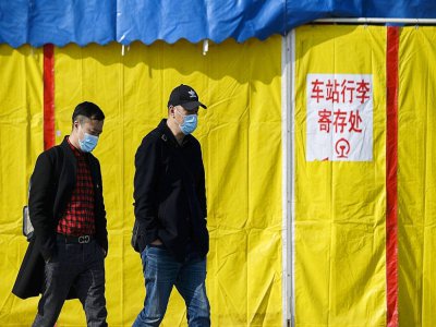 Deux hommes portant des masques de protection contre le coronavirus marchent dans une rue de Jiujiang, le 19 mars 2020 en Chine - NOEL CELIS [AFP]