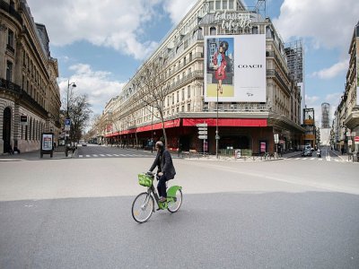 Un homme à vélo devant les Galeries Lafayette, dans un  Paris désert, le 18 mars 2020 au lendemain du début du confinement en France pour lutter contre le coronavirus - Martin BUREAU [AFP]