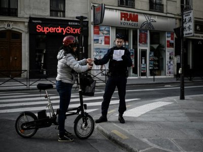 Un policier contrôle l'attestation de déplacement d'une cycliste à Paris, le 19 mars 2020 - PHILIPPE LOPEZ [AFP]