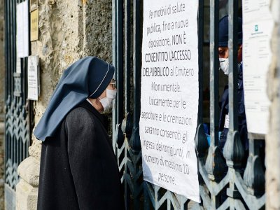 Une religieuse devant la porte d'entrée du cimetière Monumental de Bergame, fermé, le 20 mars 2020 - Piero Cruciatti [AFP]
