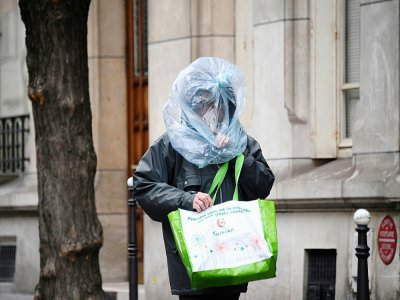 Un homme emmitouflé dans un sac en plastique, le 21 mars 2020 à Paris - FRANCK FIFE [AFP]