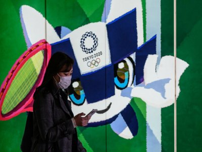 Une femme portant un masque de protection passe devant le poster de la mascotte officielle des JO 2020, le 11 mars 2020 à Tokyo - Philip FONG [AFP/Archives]