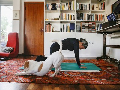 A Nicosie, une femme fait de la gym à la maison en compagnie de son chien, le 23 mars 2020 - Christina ASSI [AFP]
