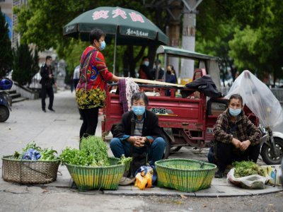 Des vendeurs de rue, le visage couvert d'un masque de protection contre le coronavirus, sur un coin de trottoir à Huanggang, dans la province chinoise du Hubei, le 26 mars 2020 - Noel Celis [AFP]