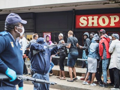 Un policier pointe son arme sur des clients d'un supermarché pour leur faire respecter la distanciation sociale, à Johannesburg, le 28 mars 2020 - MARCO LONGARI [AFP]