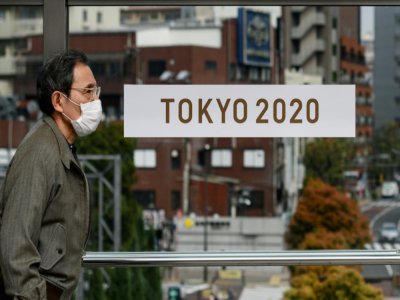 Un passant masqué devant une banderole pour les Jeux olympiques 2020 de Tokyo le 27 mars 2020 à Tokyo - Philip FONG [AFP/Archives]