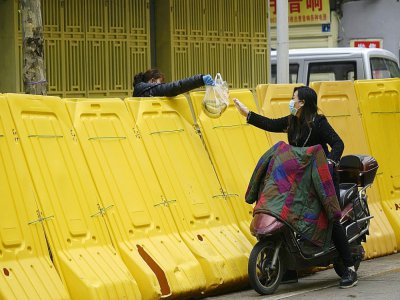 Une femme achète des bananes à une vendeuse située de l'autre côté de la barricade, à Wuhan le 2 avril 2020 - NOEL CELIS [AFP]