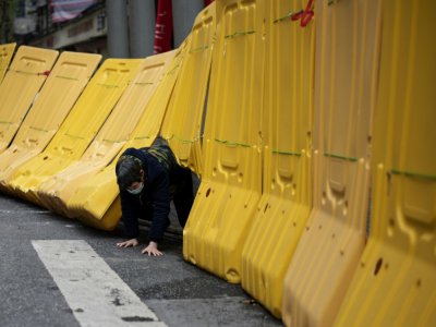 Une habitante de Wuhan, en Chine, épicentre de l'épidémie à ses débuts, passe sous une barricade, le 2 avril 2020 - NOEL CELIS [AFP]