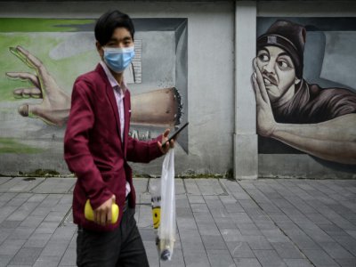 Un passant devant une fresque murale à Wuhan, en Chine, le 2 avril 2020 - NOEL CELIS [AFP]