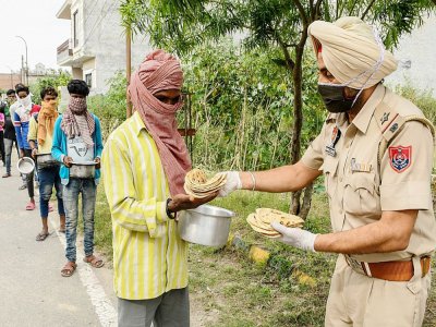 Un policier distribue de la nourriture pendant le confinement à Amritsar (Inde) le 9 avril 2020 - NARINDER NANU [AFP]