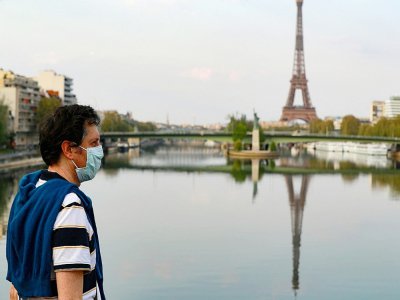 Un passant portant un masque traverse un pont sur la seine à Paris, le 11 avril 2020 - Ludovic MARIN [AFP]