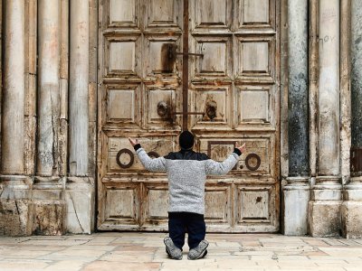 Un Chrétien prie devant les portes fermées du Saint-Sépulcre, à Jérusalem, le 9 avril 2020 - GALI TIBBON [AFP]
