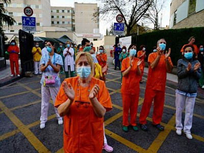 Des personnels soignants, salués par des habitants, applaudissent en retour, devant un hôpital de Madrid, le 12 avril 2020 - Pierre-Philippe Marcou [AFP]