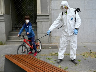 Un enfant et un employé chargé de la désinfection des rues à Madrid le 28 avril 2020 - Gabriel BOUYS [AFP]