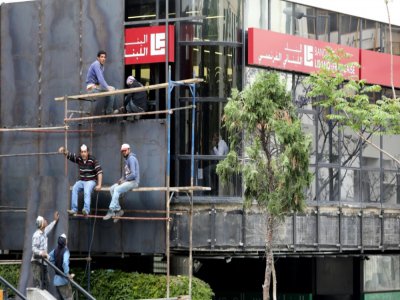Des ouvriers installent des barrières métalliques devant la façade d'une banque à Beyrouth comme mesure de protection après que des manifestants antigouvernementaux ont saccagé des banques, le 29 avril 2020 - ANWAR AMRO [AFP]