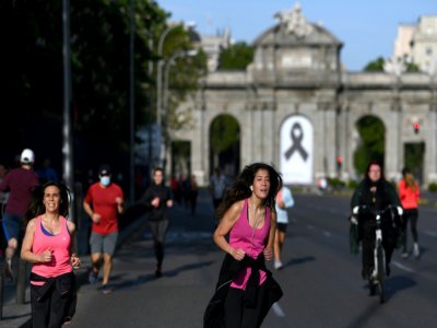 Joggeurs devant la Porte d'Alcala, ornée d'un ruban noir en signe de deuil, le 2 mai 2020 à Madrid - Gabriel BOUYS [AFP]