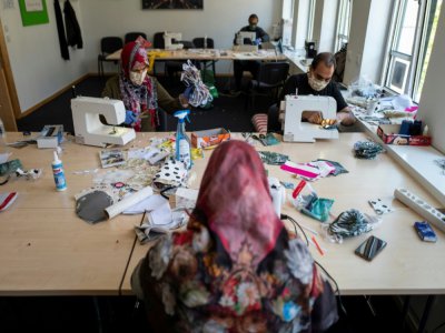 Des migrants d'Afghanistan cousent des masques de protection dans un centre communautaire, le 23 avril 2020 à Berlin, en Allemagne - John MACDOUGALL [AFP]
