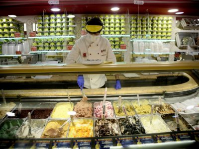 Un employé d'un magasin de glaces montre comment il respectera les mesures sanitaires lorsque l'activité reprendra, à Rome, le 30 avril 2020 - Filippo MONTEFORTE [AFP]