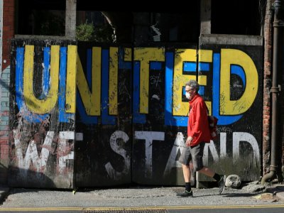 Un homme passe devant un message peint sur un mur "Nous restons unis", le 2 mai 2020 à Leeds, au Royaume-Uni - Lindsey Parnaby [AFP]