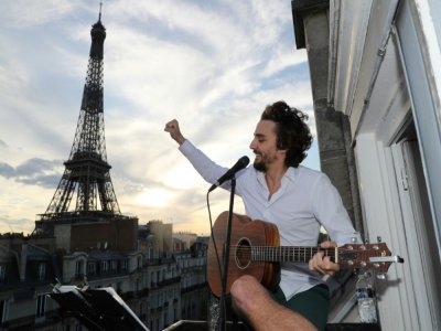 Le chanteur Adrien Pelon, dit Adril, joue sur son balcon pour ses voisins, à Paris le 2 mai 2020 - Ludovic MARIN [AFP]