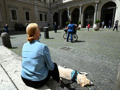 Une femme et son chien se reposent sur la place Santa Maria à Trastevere, à Rome, le 3 mai 2020. - Vincenzo PINTO [AFP]