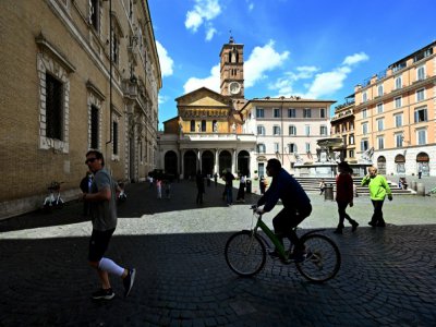 Un homme fait du vélo et un autre court, sur une place de Rome, le 3 mai 2020 - Vincenzo PINTO [AFP]