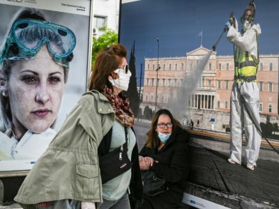 Passantes portant des masques devant une affiche, à Athènes le 4 mai 2020 - ARIS MESSINIS [AFP]