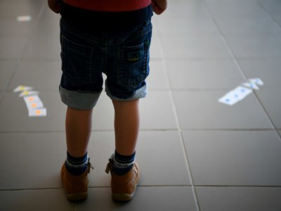 Un garçonnet découvre les flèches fixées sur le sol pour inciter à maintenir des distances de sécurité entre les enfants, dans une école des Yvelines quelques jours avant sa réouverture, le 7 mai 2020 - FRANCK FIFE [AFP]