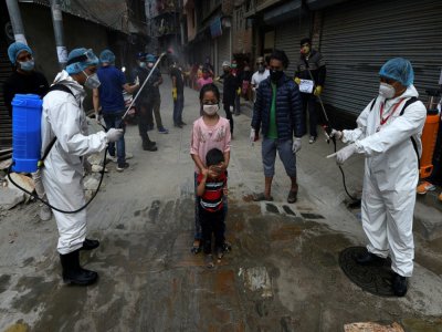 Des agents sanitaires aspergent des enfants d'une solution désinfectante, le 7 mai 2020 à Katmandou, au Népal - PRAKASH MATHEMA [AFP]
