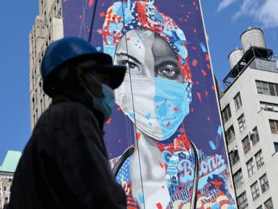 Un ouvrier masqué passe devant une fresque murale en l'honneur des soignants de la pandémie, le 7 mai 2020 à Manhattan - Angela Weiss [AFP]