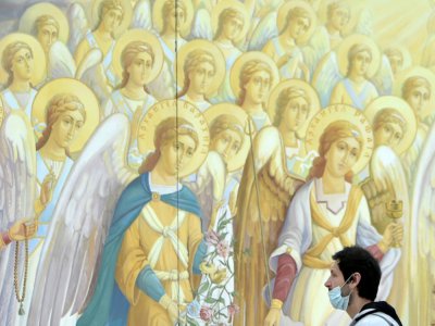 Un  homme avec masque devant une fresque religieuse du monastère Saint-Michel-au-dome-d'or, le 12 mai 2020 à Kiev, en Ukraine - Sergei SUPINSKY [AFP]