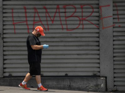 Un homme, protégé par un masque contre le coronavirus, passe devant un rideau de fer où est écrit "Faim", à Caracas, le 14 mai 2020 - Federico PARRA [AFP]